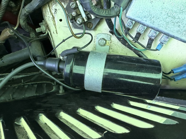 Ignition coil mounted on the inner wing of a cream MG TF 1500, with the Lucas fuse box and control box nearby